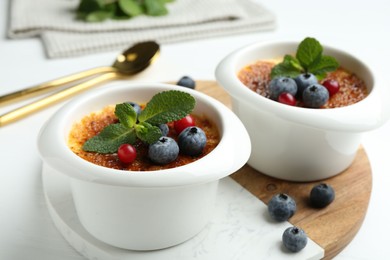 Delicious creme brulee with berries and mint in bowls on white table, closeup