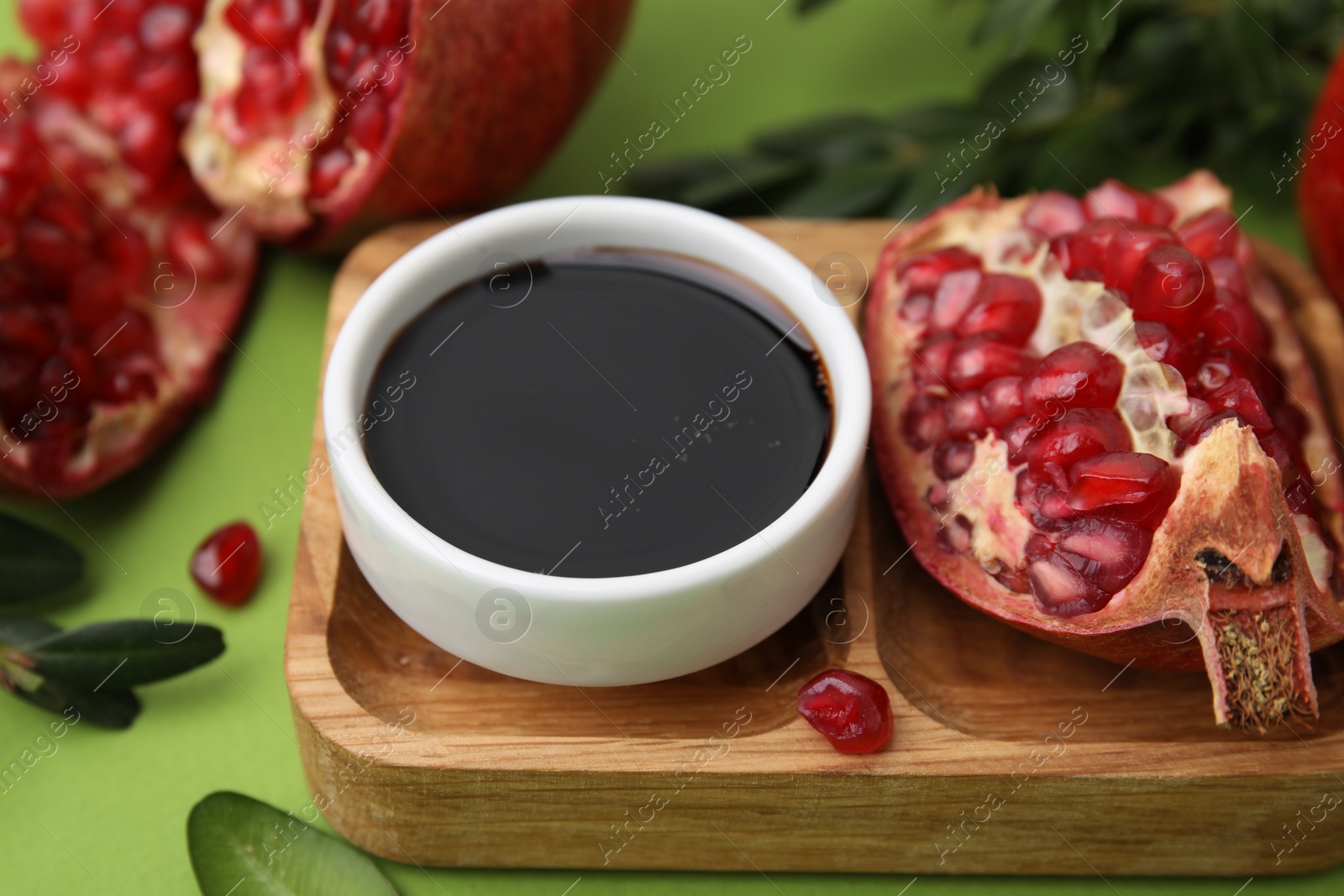 Photo of Tasty pomegranate sauce in bowl and fruits on green table, closeup