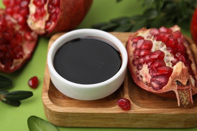 Photo of Tasty pomegranate sauce in bowl and fruits on green table, closeup