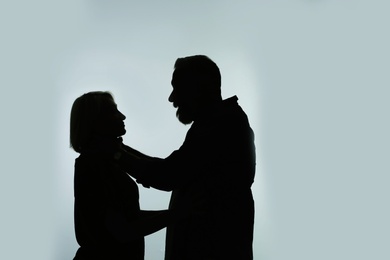 Photo of Silhouette of man strangling his wife on color background. Relationship problems
