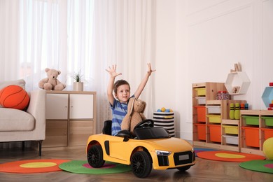 Little child with bunny sitting in toy car indoors