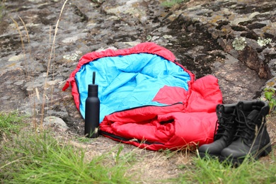 Photo of Sleeping bag, boots and bottle outdoors. Camping gear