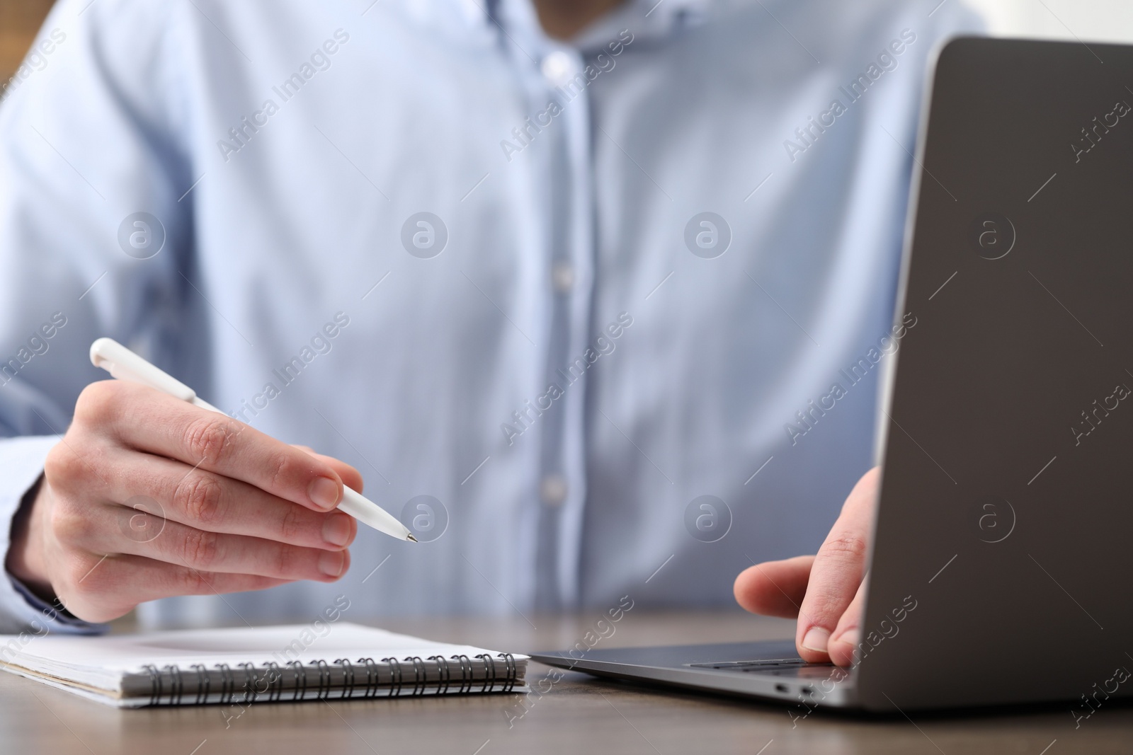 Photo of E-learning. Man taking notes during online lesson at table indoors, closeup