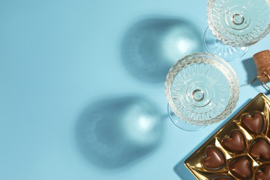 Photo of Glasses of expensive white wine, cork and heart shaped chocolate candies on light blue background, flat lay. Space for text