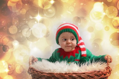 Image of Cute baby in elf costume near wicker basket against blurred festive lights. Christmas celebration
