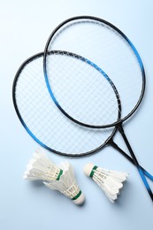 Photo of Feather badminton shuttlecocks and rackets on light blue background, flat lay