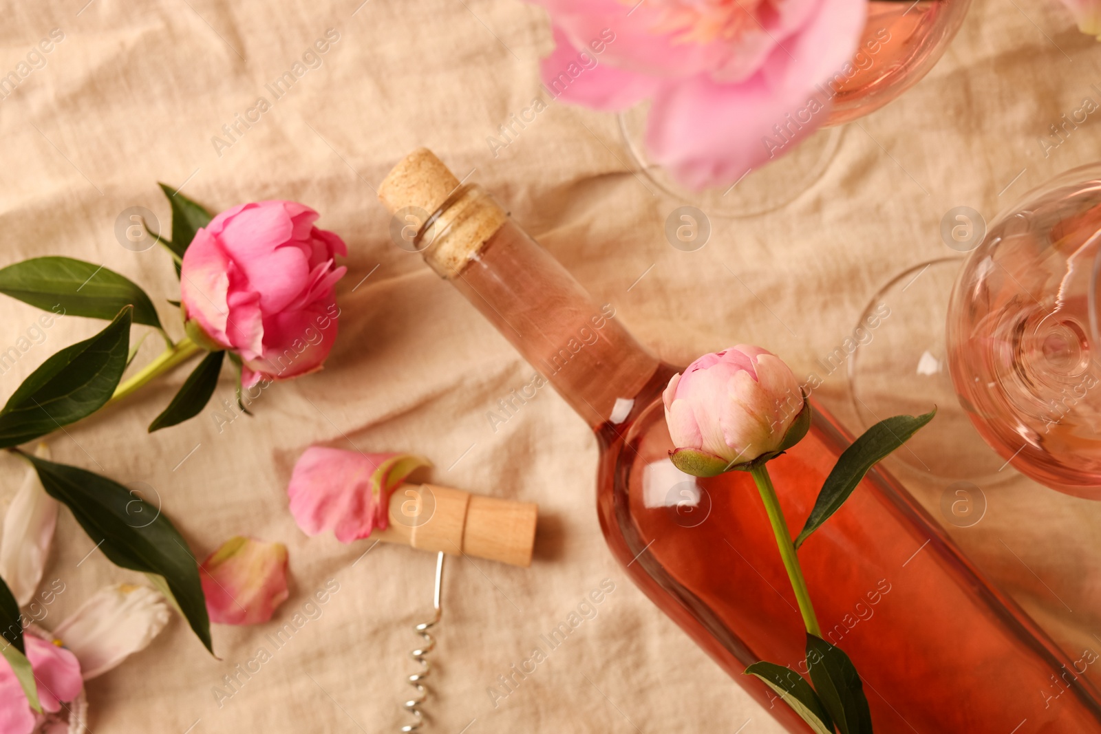 Photo of Flat lay composition with rose wine and beautiful peonies on beige fabric