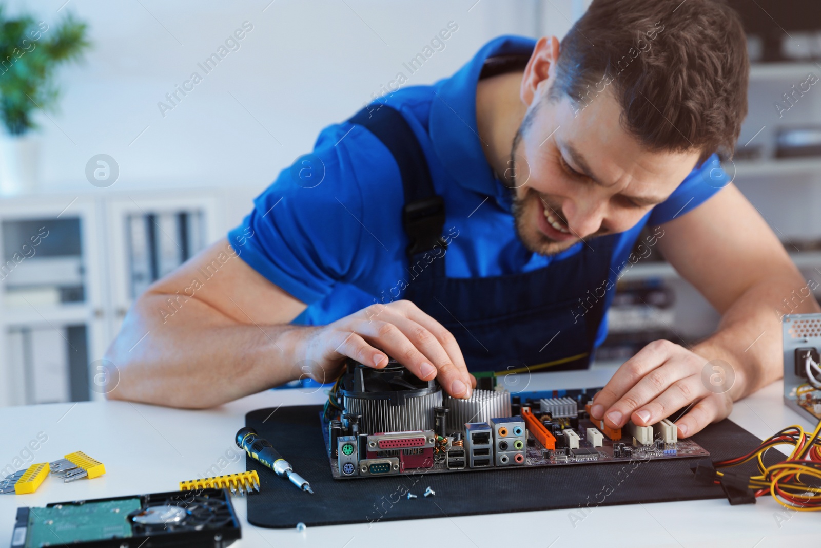 Photo of Male technician repairing motherboard at table indoors