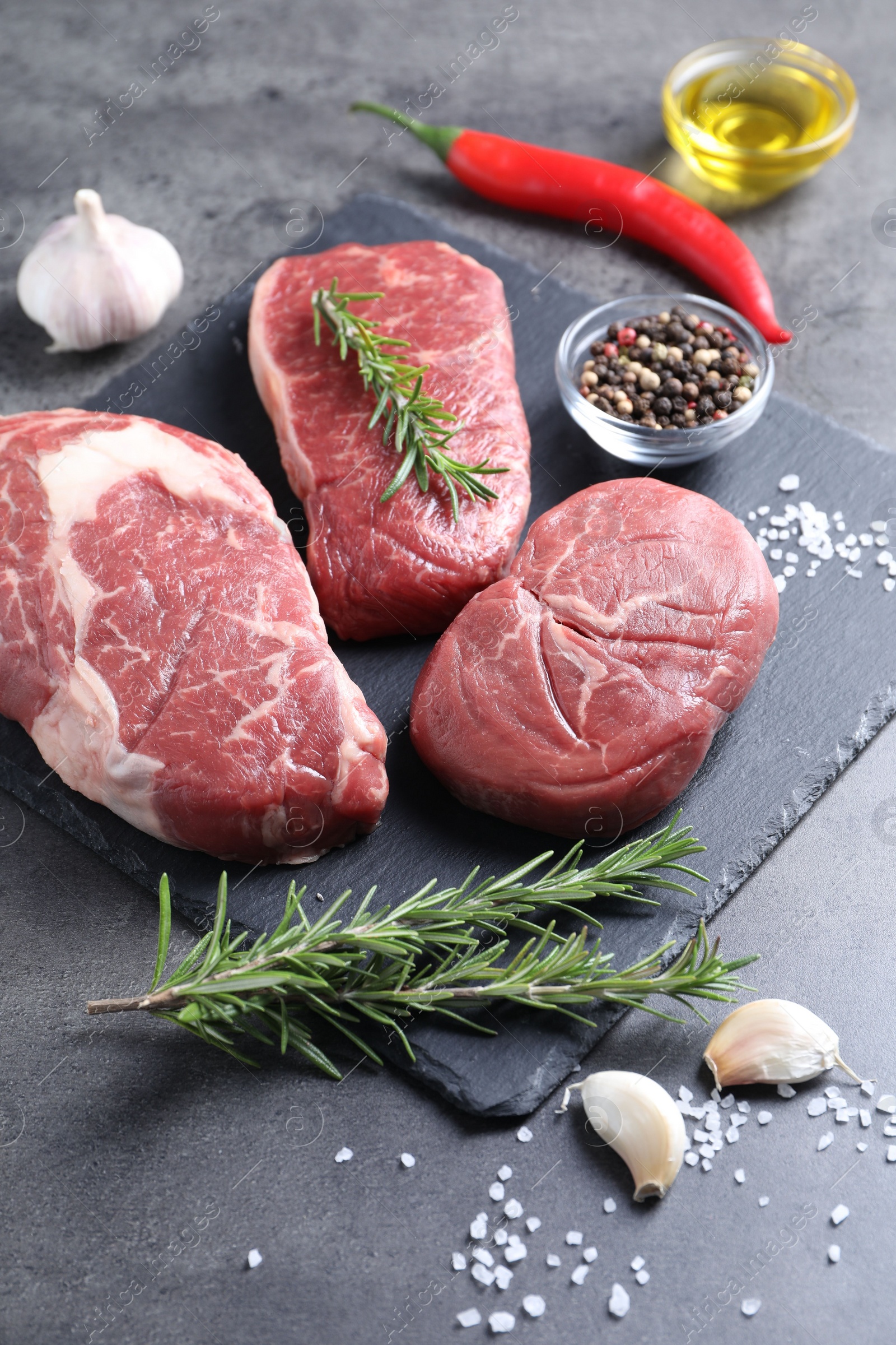 Photo of Raw beef steaks, oil and spices on grey background, closeup