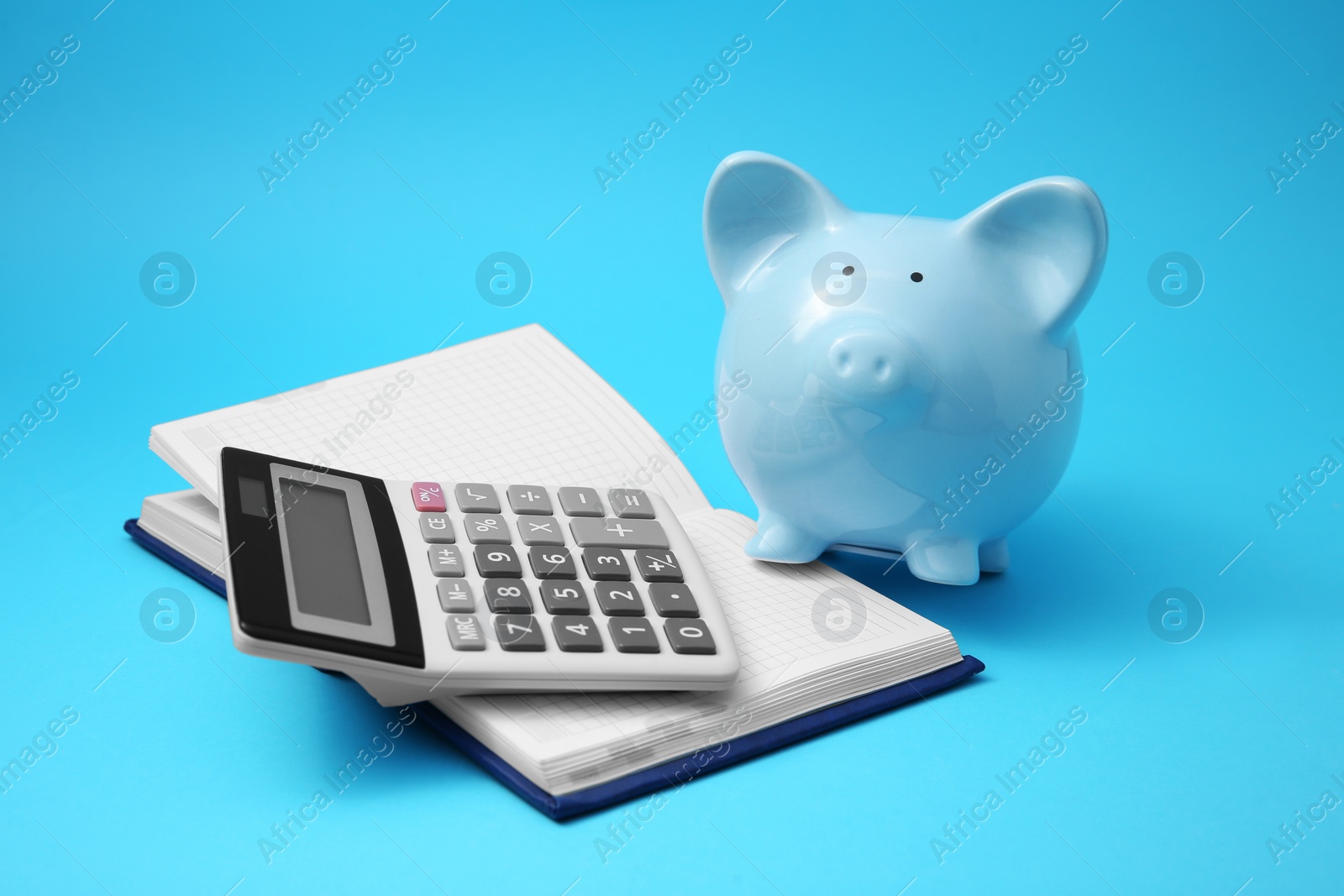 Photo of Piggy bank, notebook and calculator on light blue background