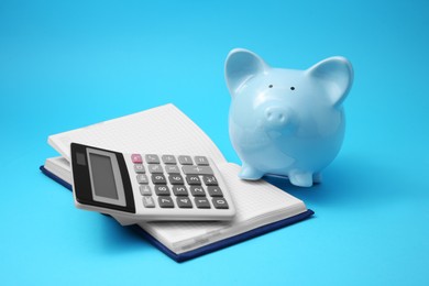 Photo of Piggy bank, notebook and calculator on light blue background