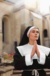 Young nun with hands clasped together praying near building outdoors