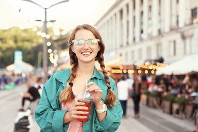 Photo of Young woman with refreshing drink on city street. Space for text