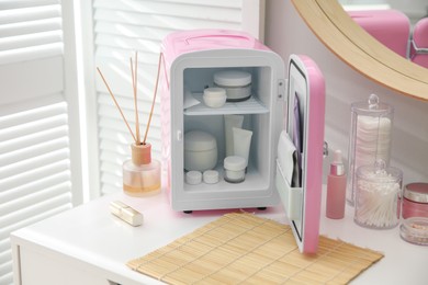 Photo of Cosmetics refrigerator and skin care products on white vanity table indoors