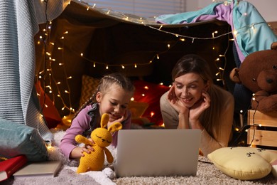 Mother and her daughter with laptop in play tent at home