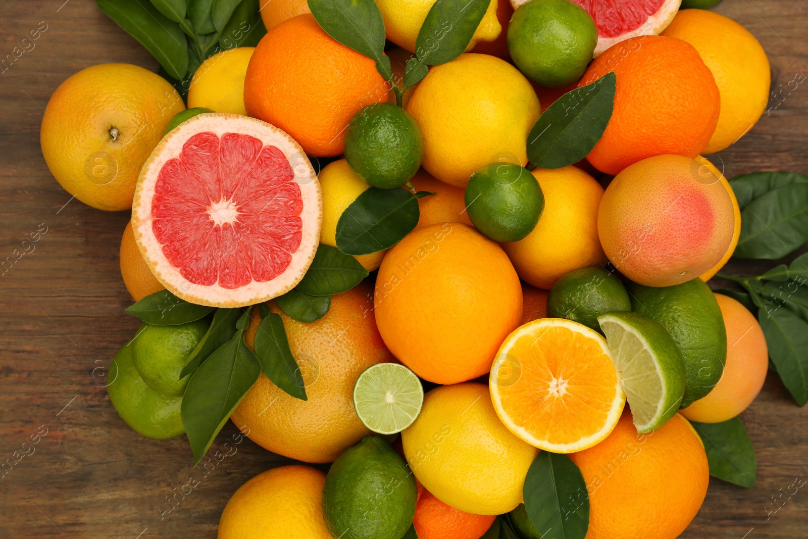 Photo of Different citrus fruits with green leaves on wooden table, flat lay