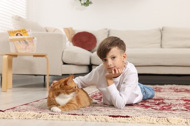 Photo of Little boy petting cute ginger cat on carpet at home