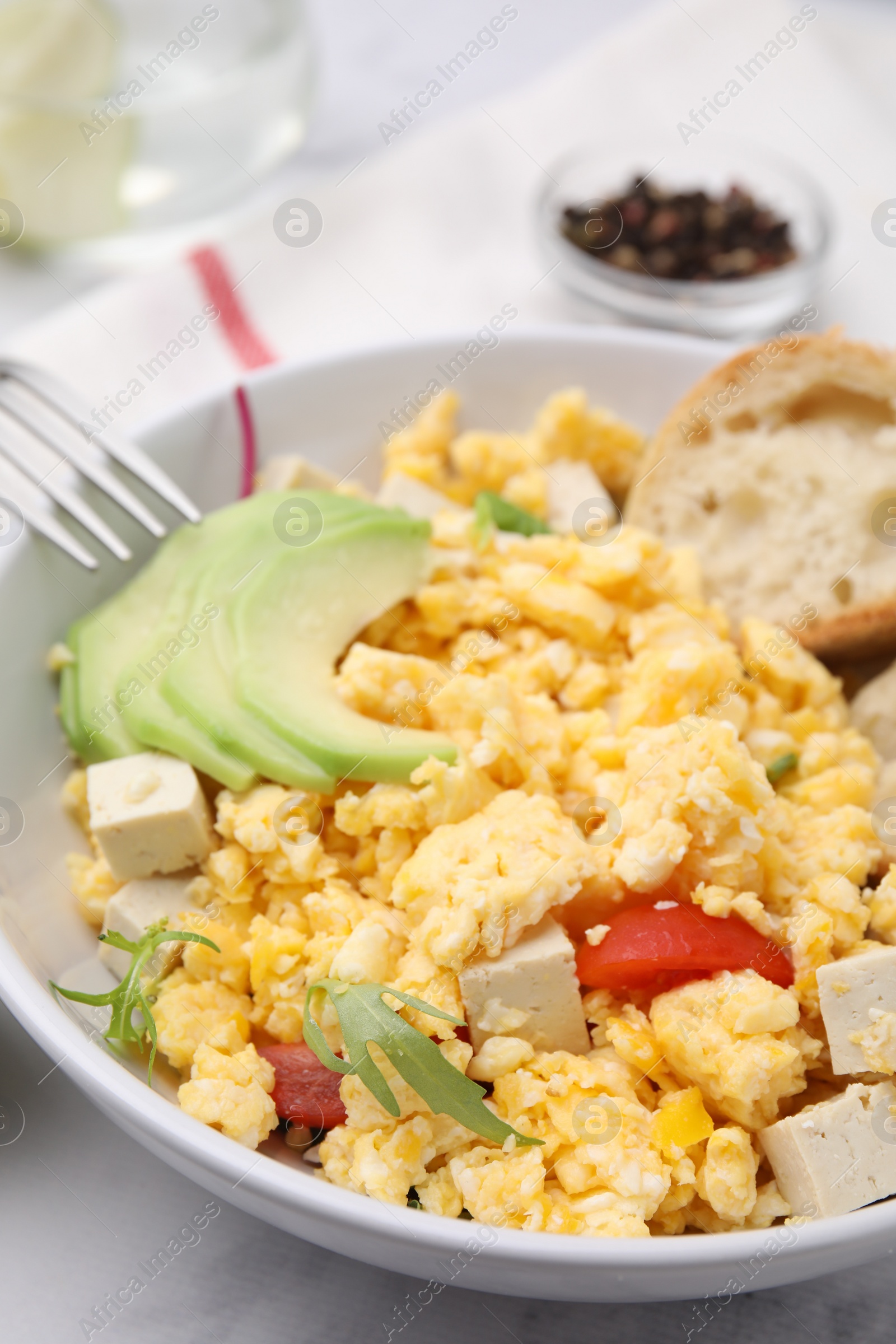 Photo of Bowl with delicious scrambled eggs, tofu and avocado on white table, closeup