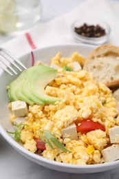 Bowl with delicious scrambled eggs, tofu and avocado on white table, closeup