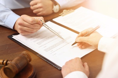 Image of Lawyer pointing at document and client putting signature at wooden table in office, closeup