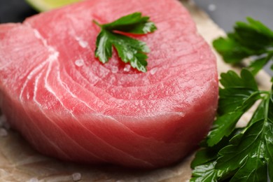 Photo of Fresh raw tuna fillet with sea salt and parsley on table, closeup