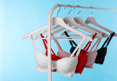 Photo of Hangers with beautiful lace bras on rack against blue background. Stylish underwear