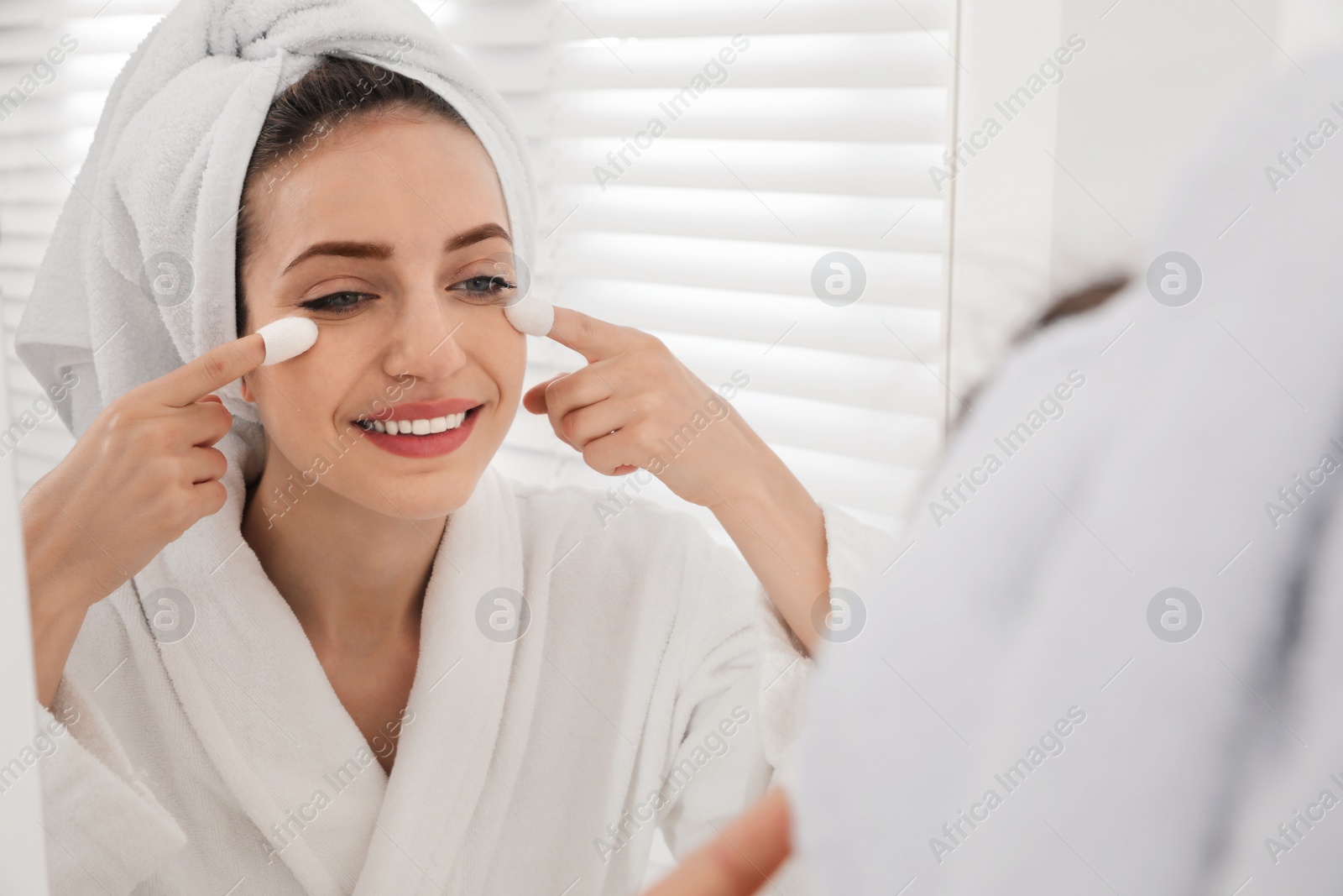 Photo of Woman using silkworm cocoons in skin care routine near mirror at home