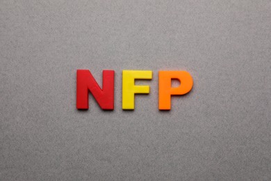 Photo of Abbreviation NFP (Nonfarm Payroll) made of letters on grey background, top view