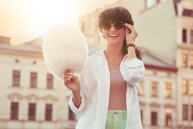 Image of Smiling woman with cotton candy in city on sunny day