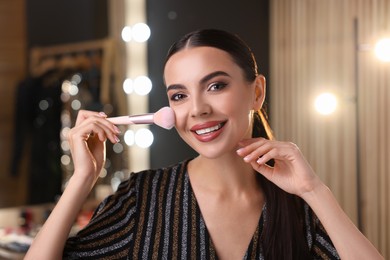 Photo of Bright makeup. Beautiful woman applying face powder in dressing room