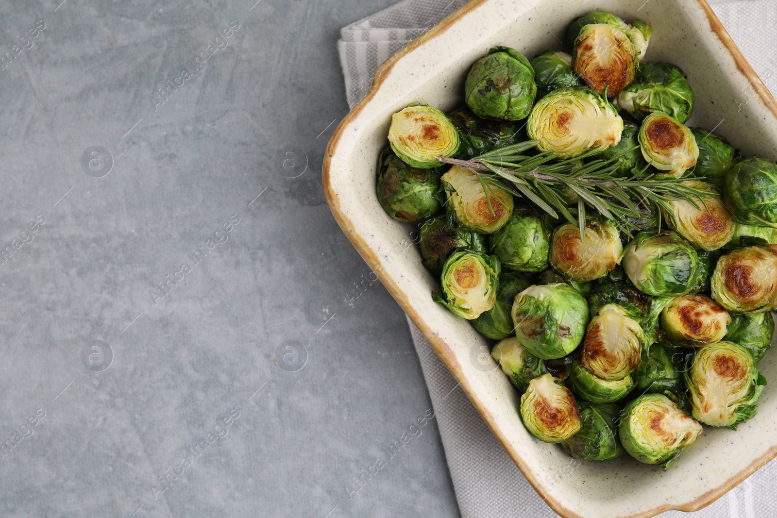 Photo of Delicious roasted Brussels sprouts and rosemary in baking dish on grey table, top view. Space for text