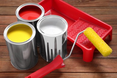 Cans of paints, roller and tray on wooden table