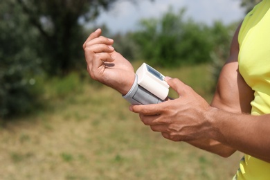 Photo of Young man checking pulse with medical device after training in park, closeup