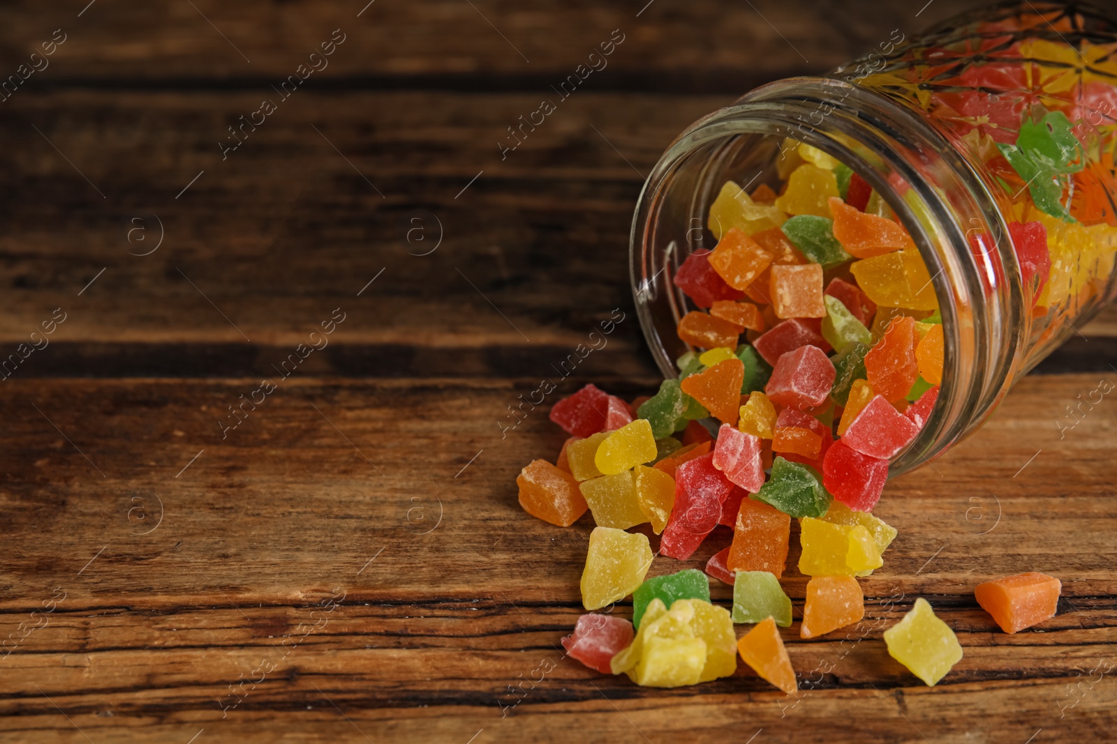 Photo of Overturned jar with mix of delicious candied fruits on wooden table. Space for text