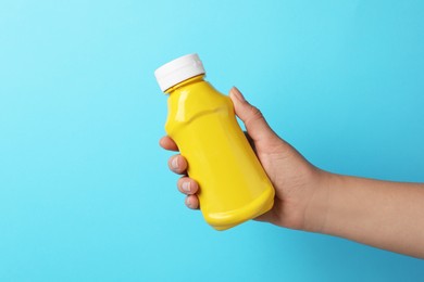 Photo of Woman with bottle of mustard on light blue background, closeup