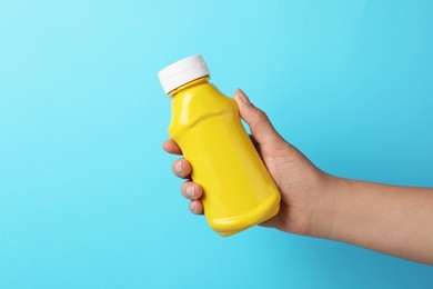 Woman with bottle of mustard on light blue background, closeup