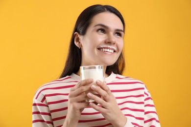 Happy woman with milk mustache holding glass of tasty dairy drink on yellow background