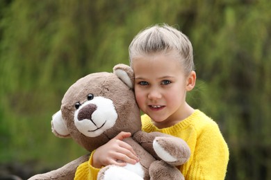 Photo of Cute little girl with teddy bear outdoors