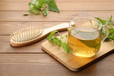 Photo of Stinging nettle infusion, leaves and brush on wooden table. Natural hair care