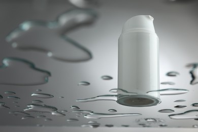 Moisturizing cream in bottle on glass with water drops against grey background, low angle view. Space for text