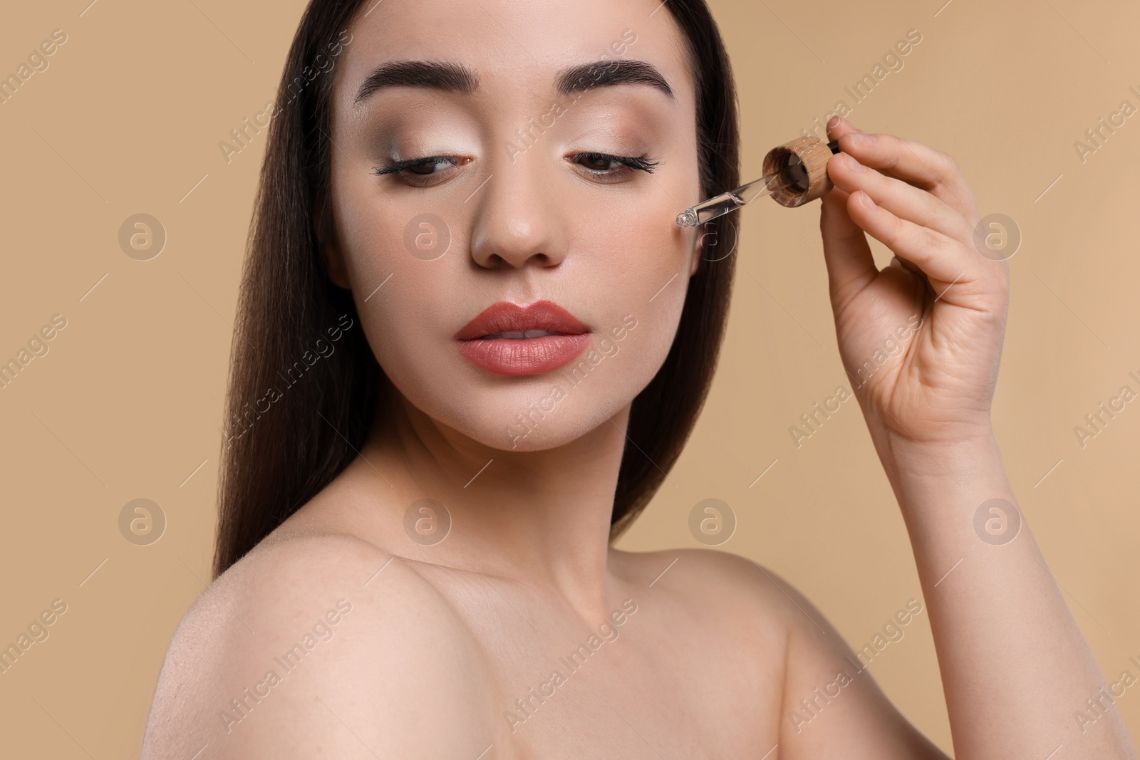 Photo of Young woman applying essential oil onto face on beige background