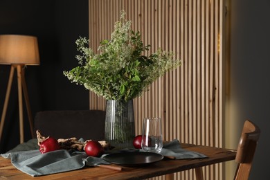 Photo of Set of clean dishware, ripe red apples and flowers on wooden table in stylish dining room