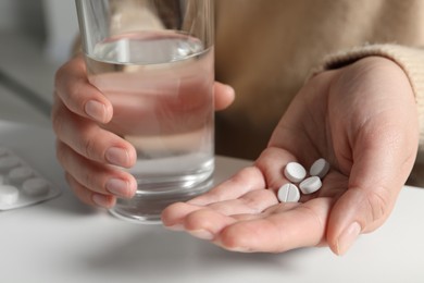 Photo of Woman with glass of water and pills at white table, closeup
