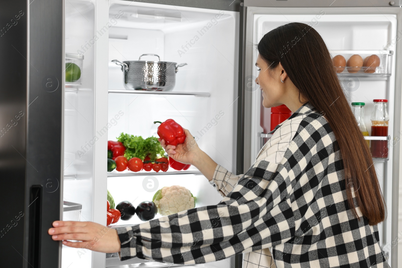 Photo of Young woman taking red bell pepper out of refrigerator