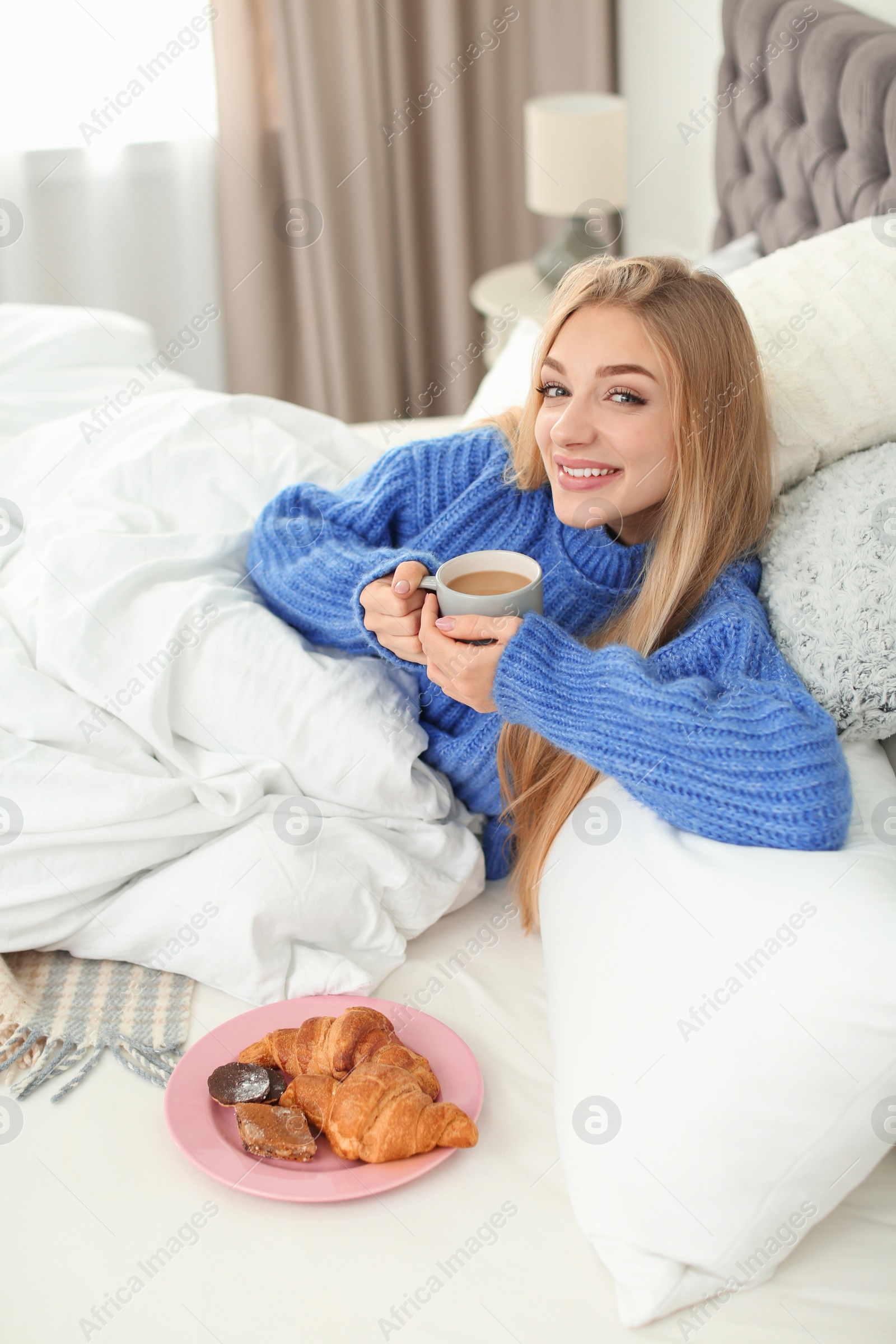 Photo of Beautiful young woman lying with breakfast in bed at home. Winter atmosphere