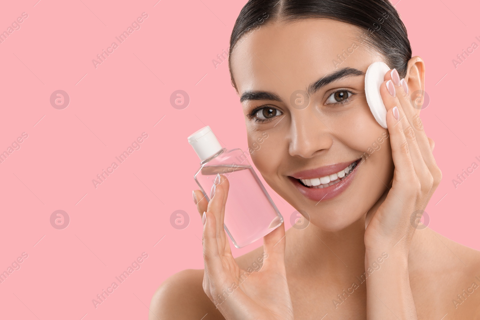 Photo of Beautiful woman removing makeup with cotton pad on pink background. Space for text