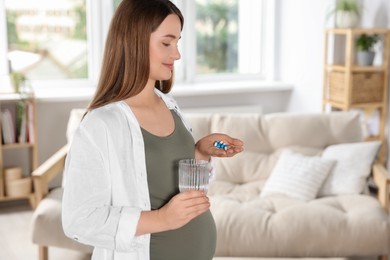 Photo of Beautiful pregnant woman holding pile of pills and glass with water at home