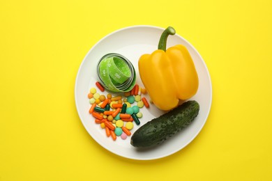Photo of Plate with weight loss pills, vegetables and measuring tape on yellow background, top view