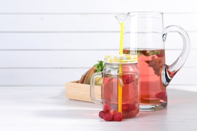 Mason jar and jug of tasty rhubarb cocktail with raspberry on white wooden table, space for text