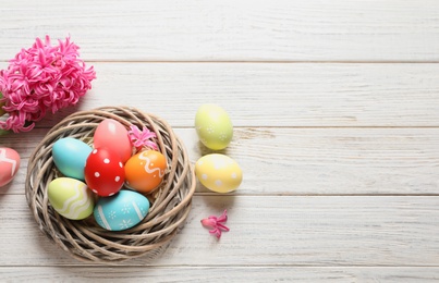 Flat lay composition of wicker nest with colorful painted Easter eggs and flower on table, space for text